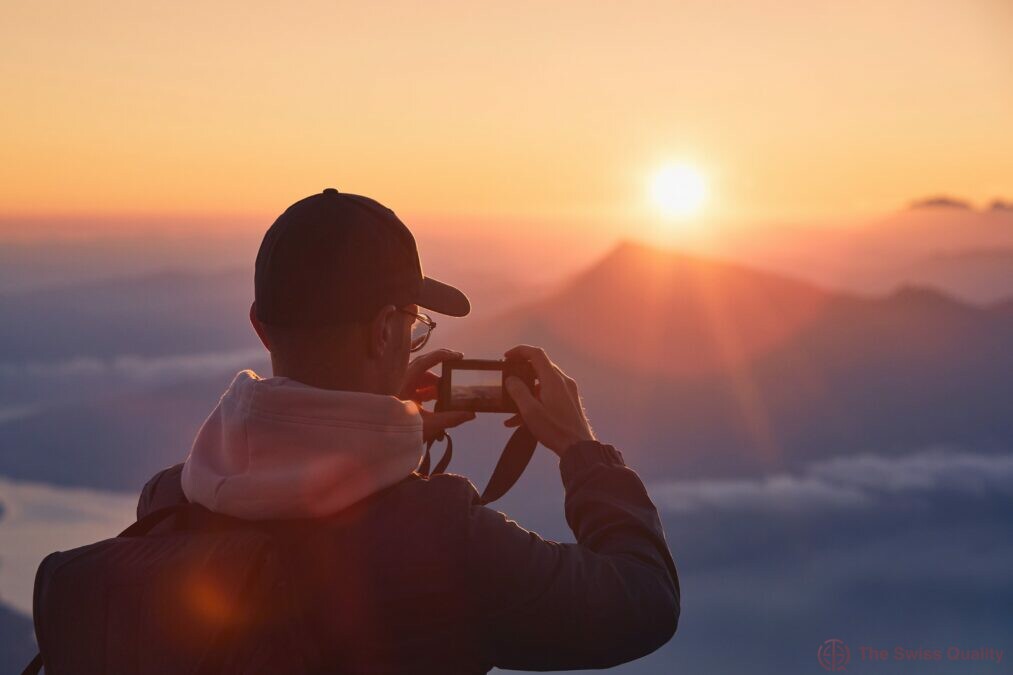 young man on top of mountain photographing sun under horizon lucerne switzerland